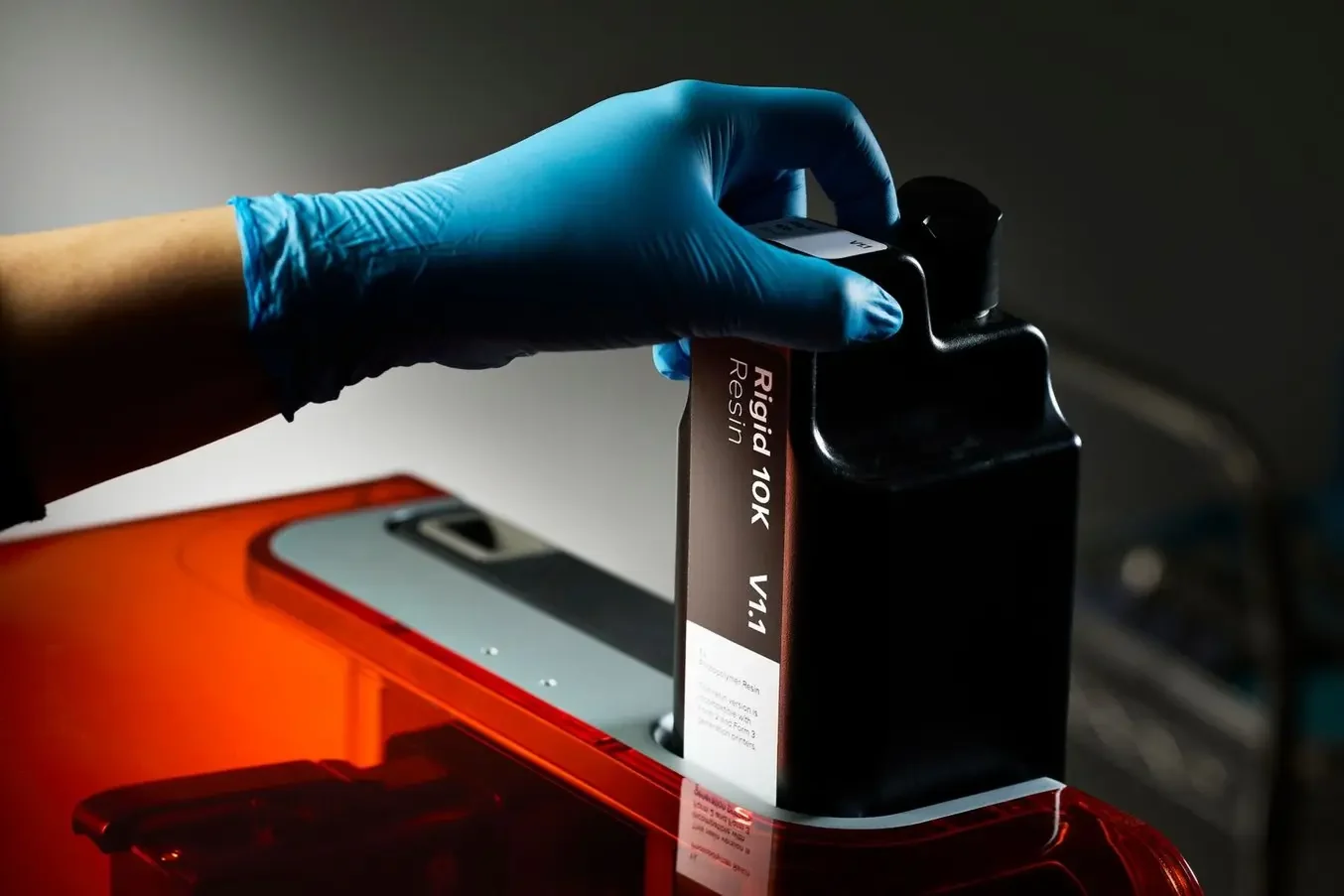 A gloved hand seating a sealed Rigid 10K resin cartridge on a Form 4