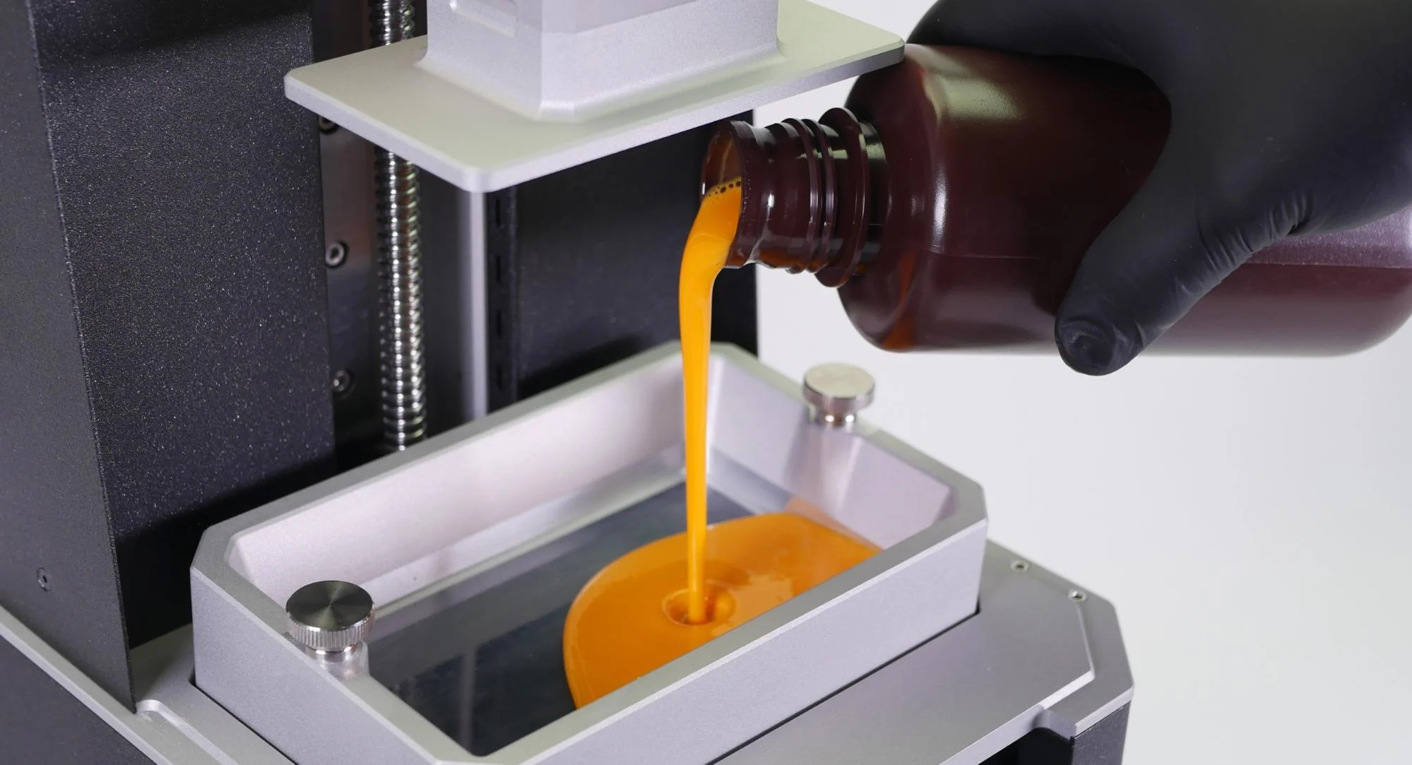 Amber low-cost resin being poured by hand from a brown bottle into an open resin vat