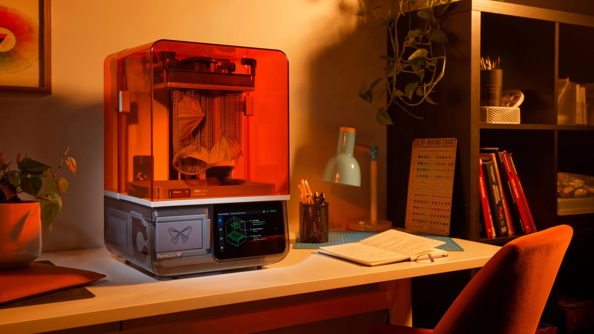Form Studio 1 printing a dragon on a desk at home in warm evening light, beside a lamp and an open notebook