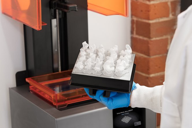 A technician holding a build platform full of 3D printed ear molds